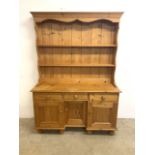 A pine kitchen dresser with breakfront base with cupboard and drawers top with two plate racks. W: