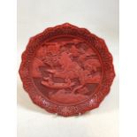 An oriental cinnabar style lacquer plate with scene of figures in a boat, with scrolled foliate