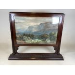 A late 19th early 20th century mahogany glazed screen with fret carved base, with coloured landscape