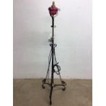 A wrought iron adjustable standard lamp with cranberry glass oil lamp - converted to electric -