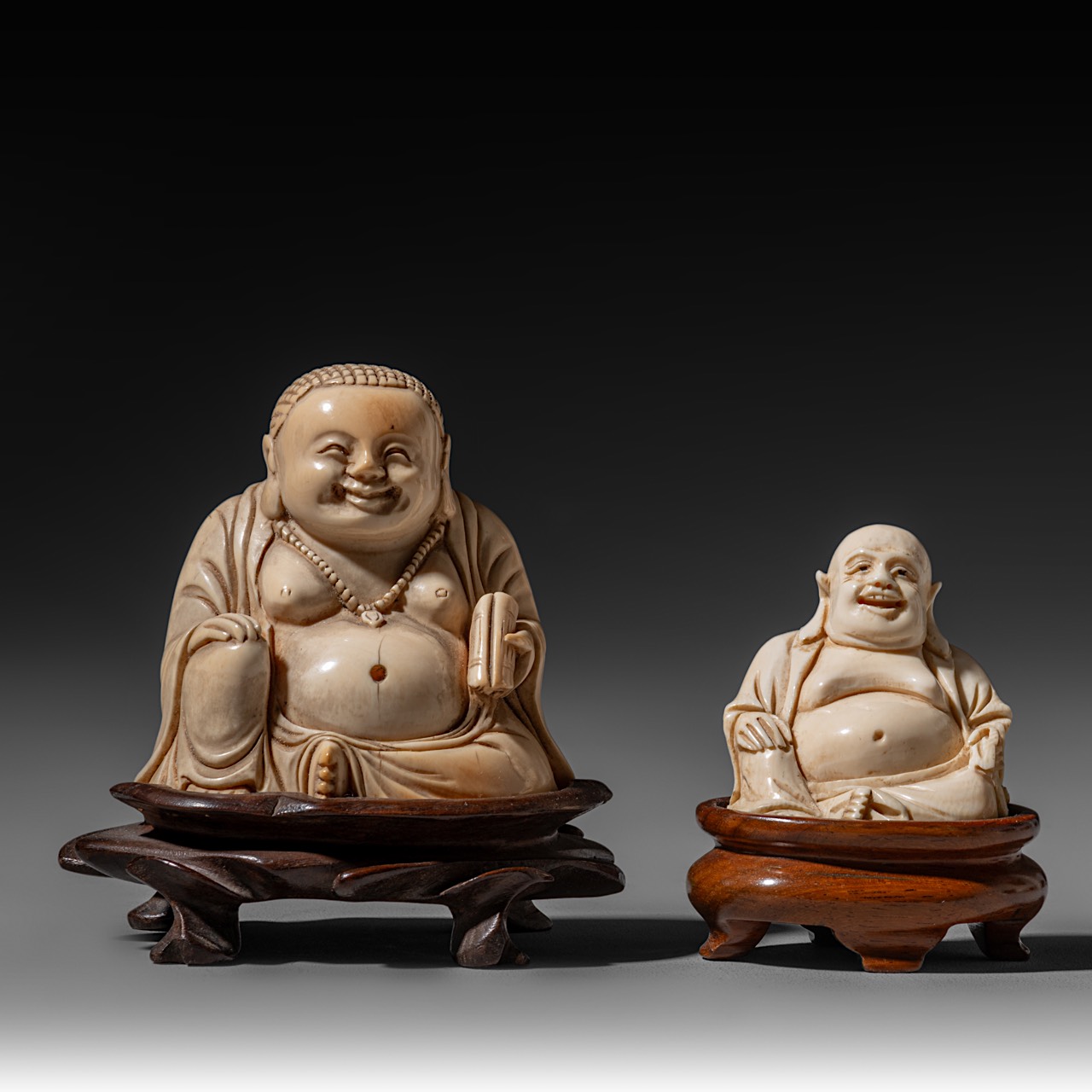 Two ivory sitting Budai figures, the smallest of them walrus ivory, both on a wooden base, H 5,3 - 7
