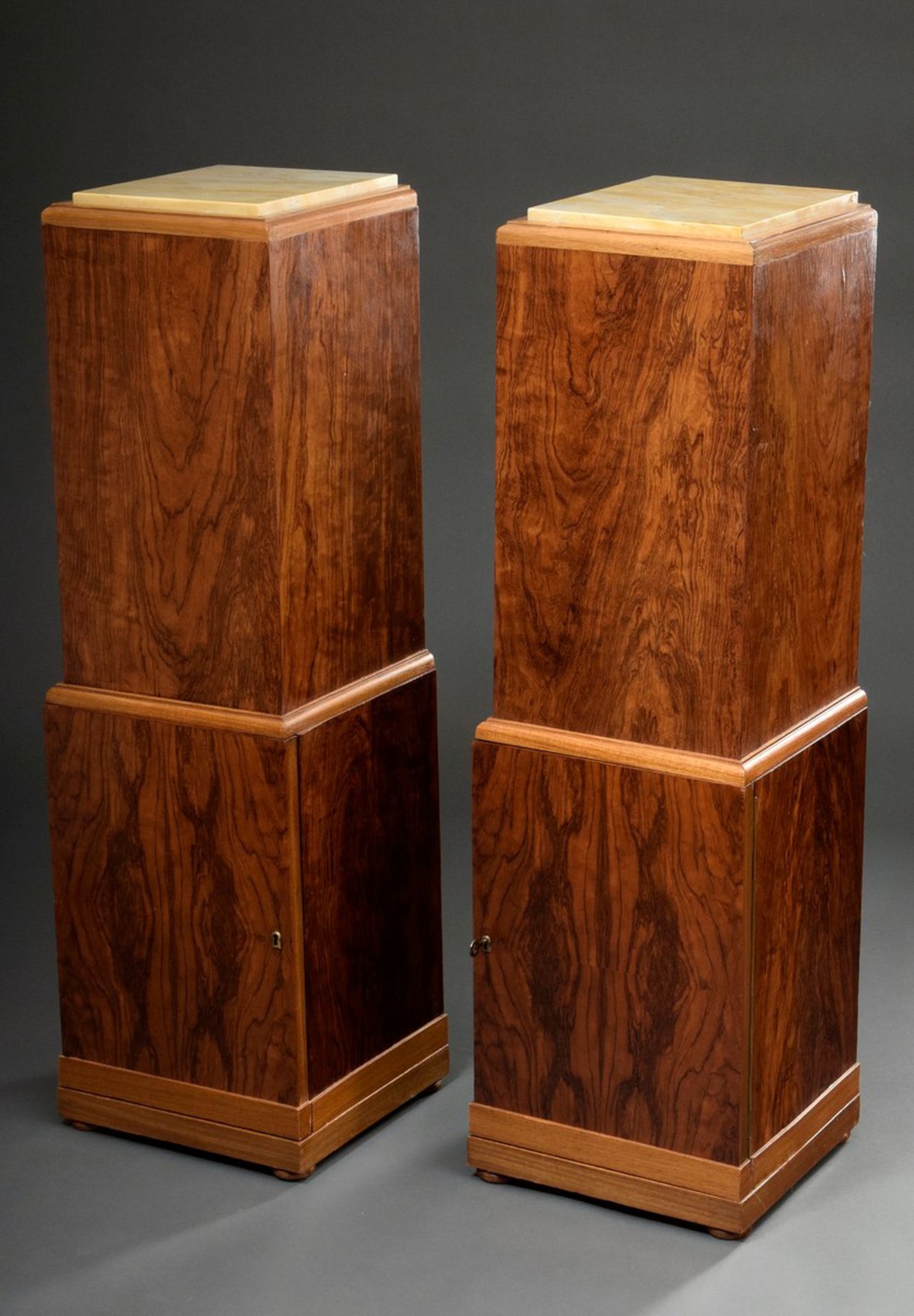 Pair of angular Art Deco columned cabinets with light marble tops, each with a lockable compartment