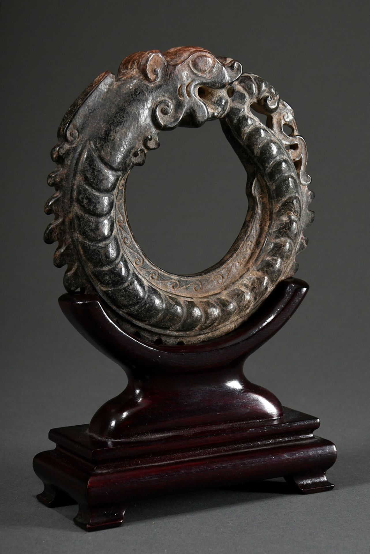 Dark jade carving "Round-laid dragon", powerfully stylised with jagged back and scales, wooden stan