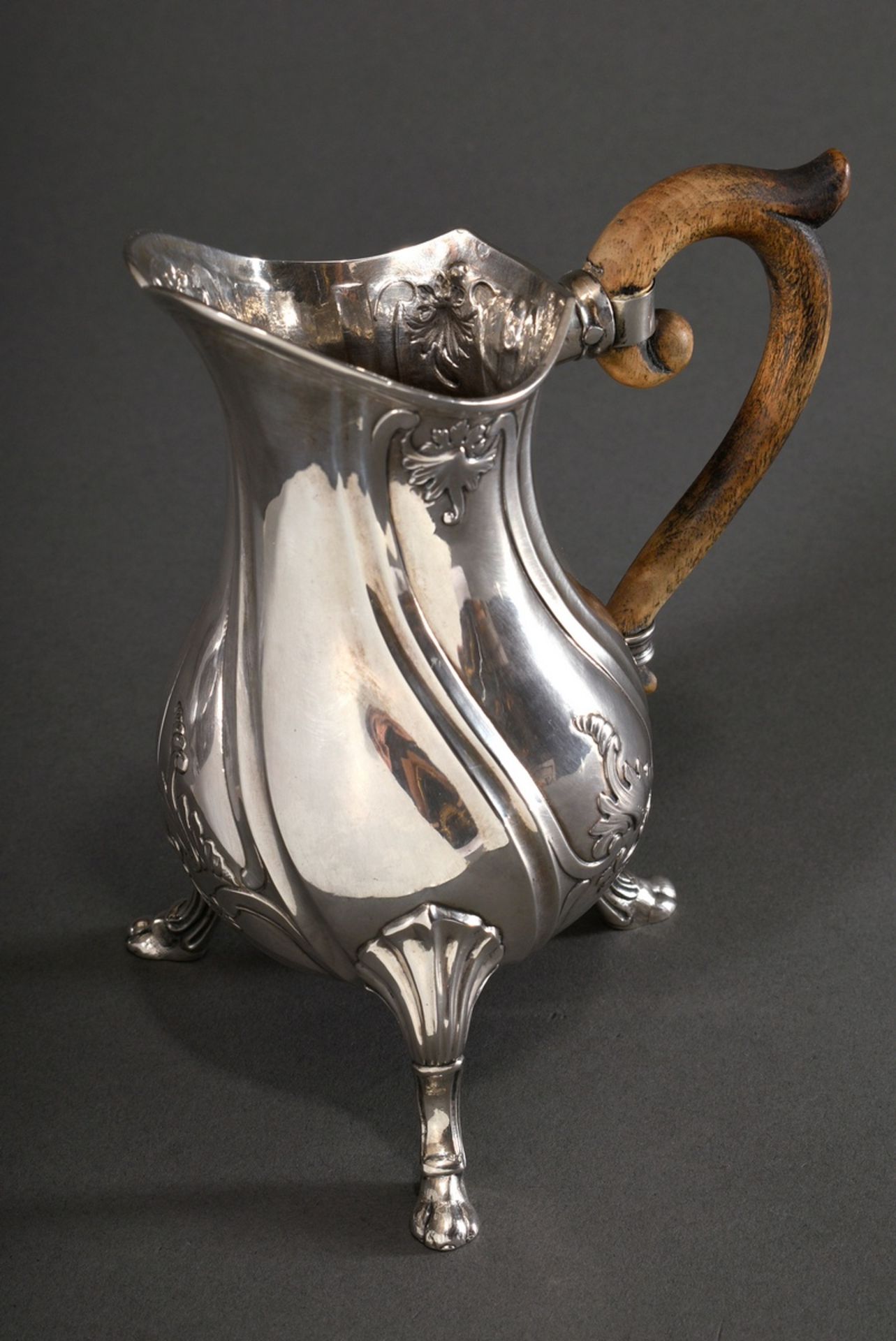 Elegant milk jug with curved wooden handle on paw feet with rocaille reliefs over curved features, 