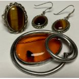 A silver coloured metal and amber set brooch; a silver coloured metal tigers eye ring and