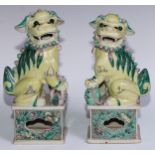 A pair of Chinese porcelain models of temple dogs, decorated in tones of yellow, green and