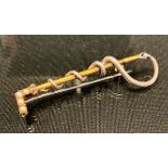 A gold and silver coloured metal riding crop brooch, the handle set with four seed pearls and