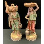 A pair of Royal Dux figures, Persian Water Carriers, both standing, in washed tones, picked out in