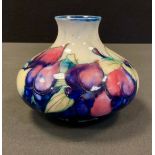 A Moorcroft Wisteria pattern compressed ovoid vase, tube lined with foliage, in tones of purple,