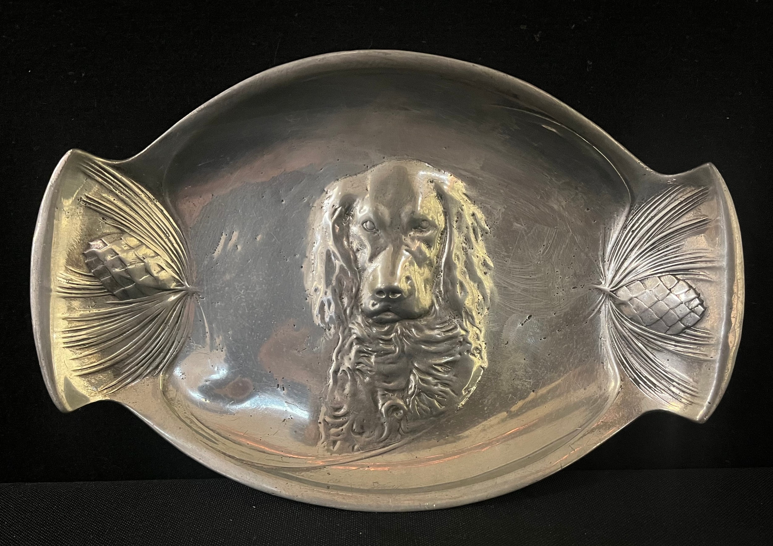 A W.M.F. plated pewter shaped oval dish, embossed with a Retriever, the handles with pine cones