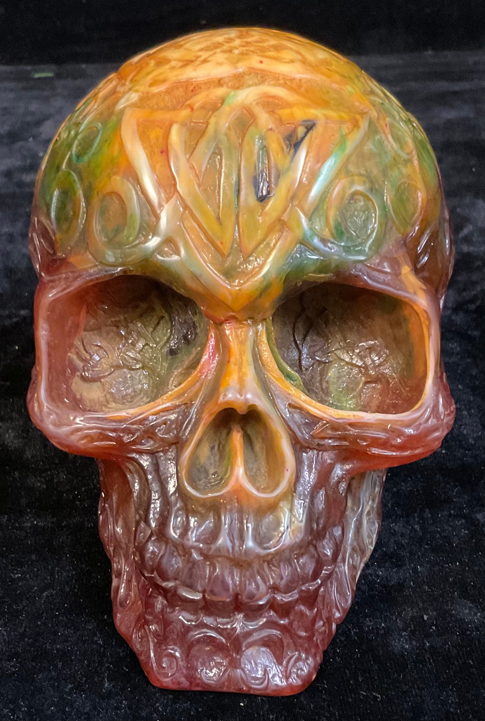 An amber coloured resin skull, cast with Celtic style scrolling decoration, 13cm high