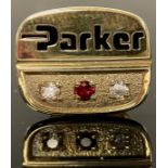 A 9ct gold pin badge, Parker employee award, set with a ruby chip flanked by a pair of diamond