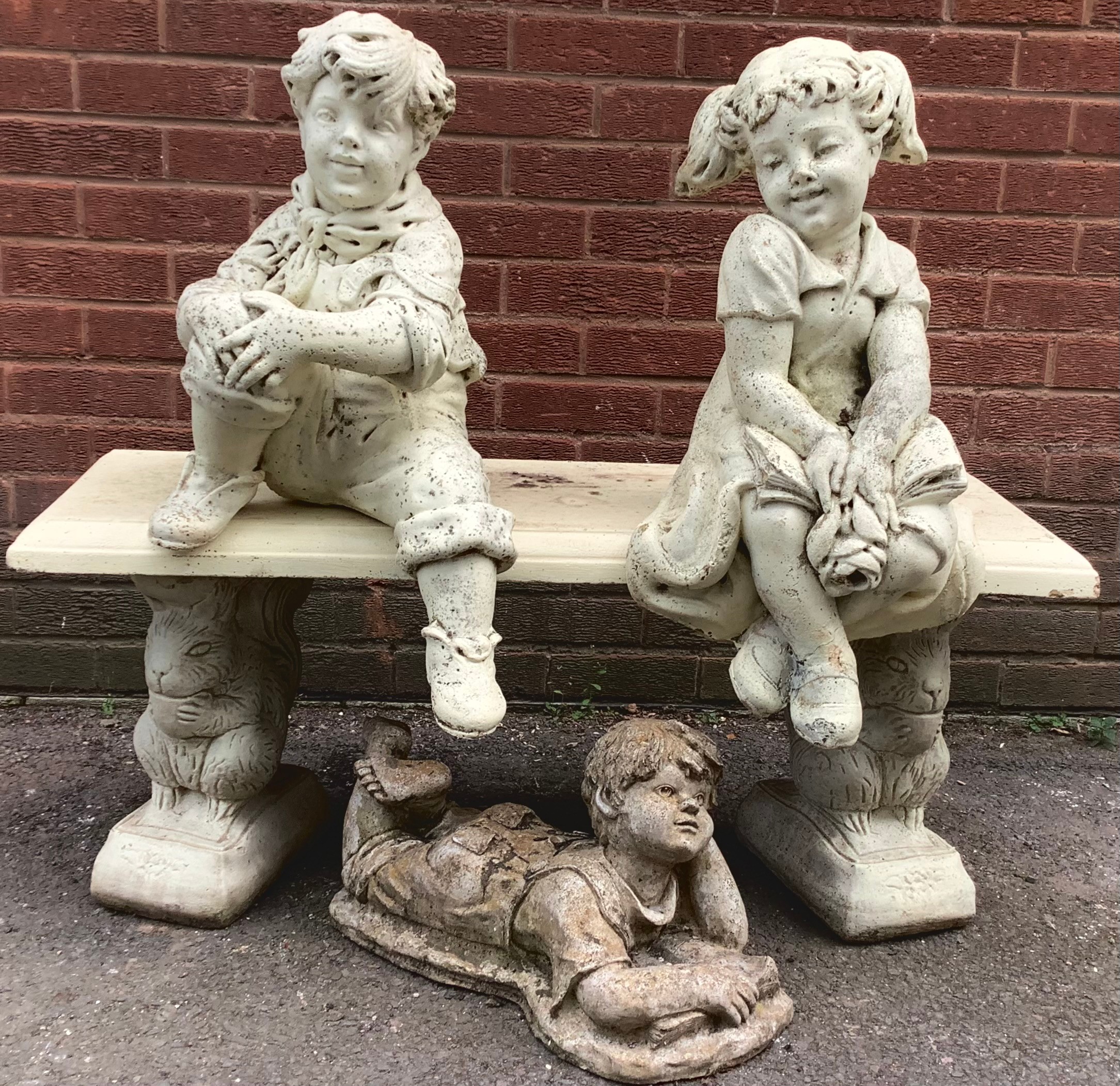 A decorative reconstituted stone model of a boy and girl, sat upon a bench, the supports modelled as