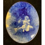 A Doulton Burslem oval plaque, printed and painted in blue with child and doll seated on a log