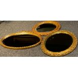 A gilt oval mirror, the frame pierced with scrolls, 62cm wide; another, Globe, 72cm wide; a circular