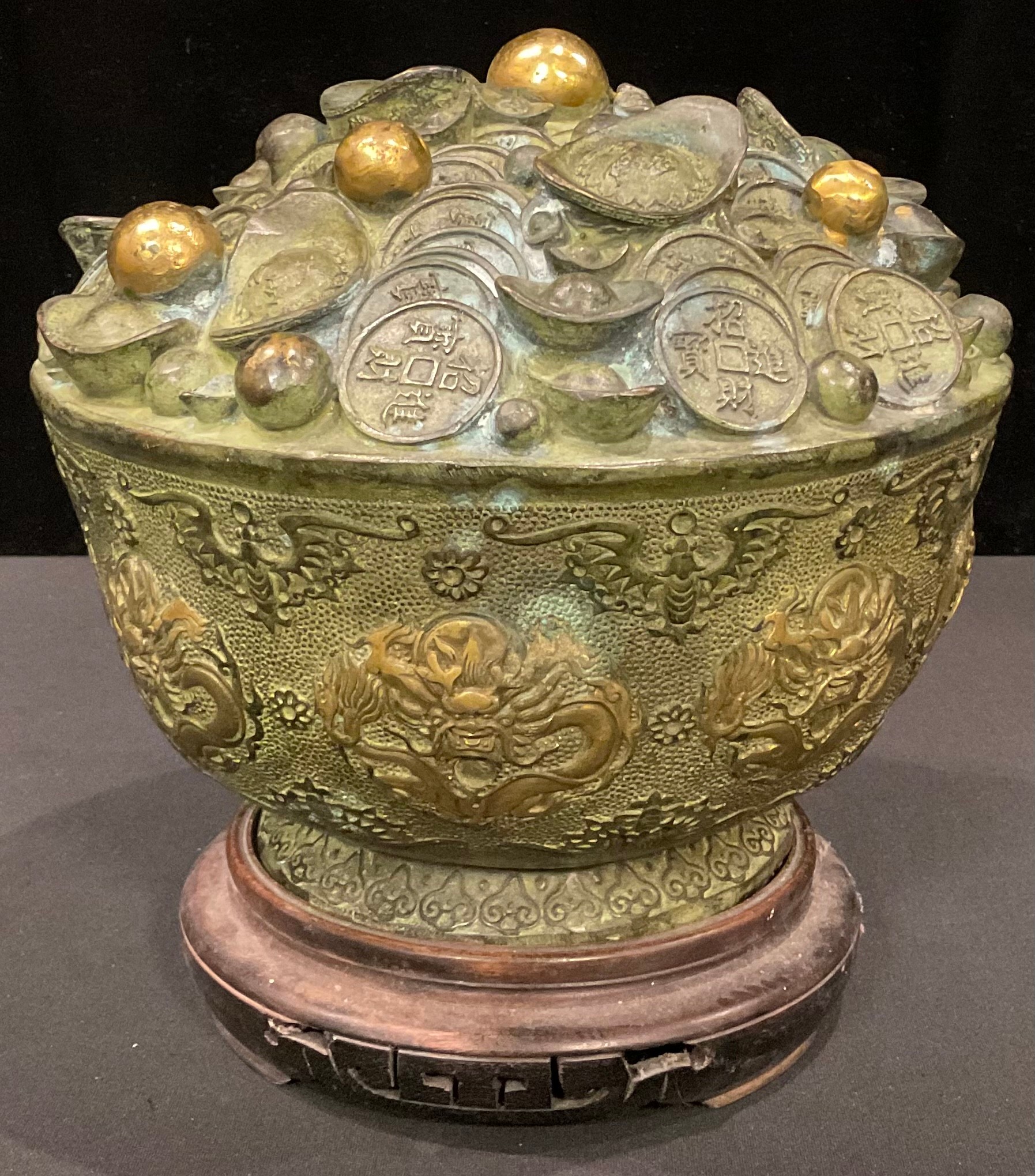 A Chinese bronzed metal fortune or treasure bowl, decorated with dragons and bats, on hardwood