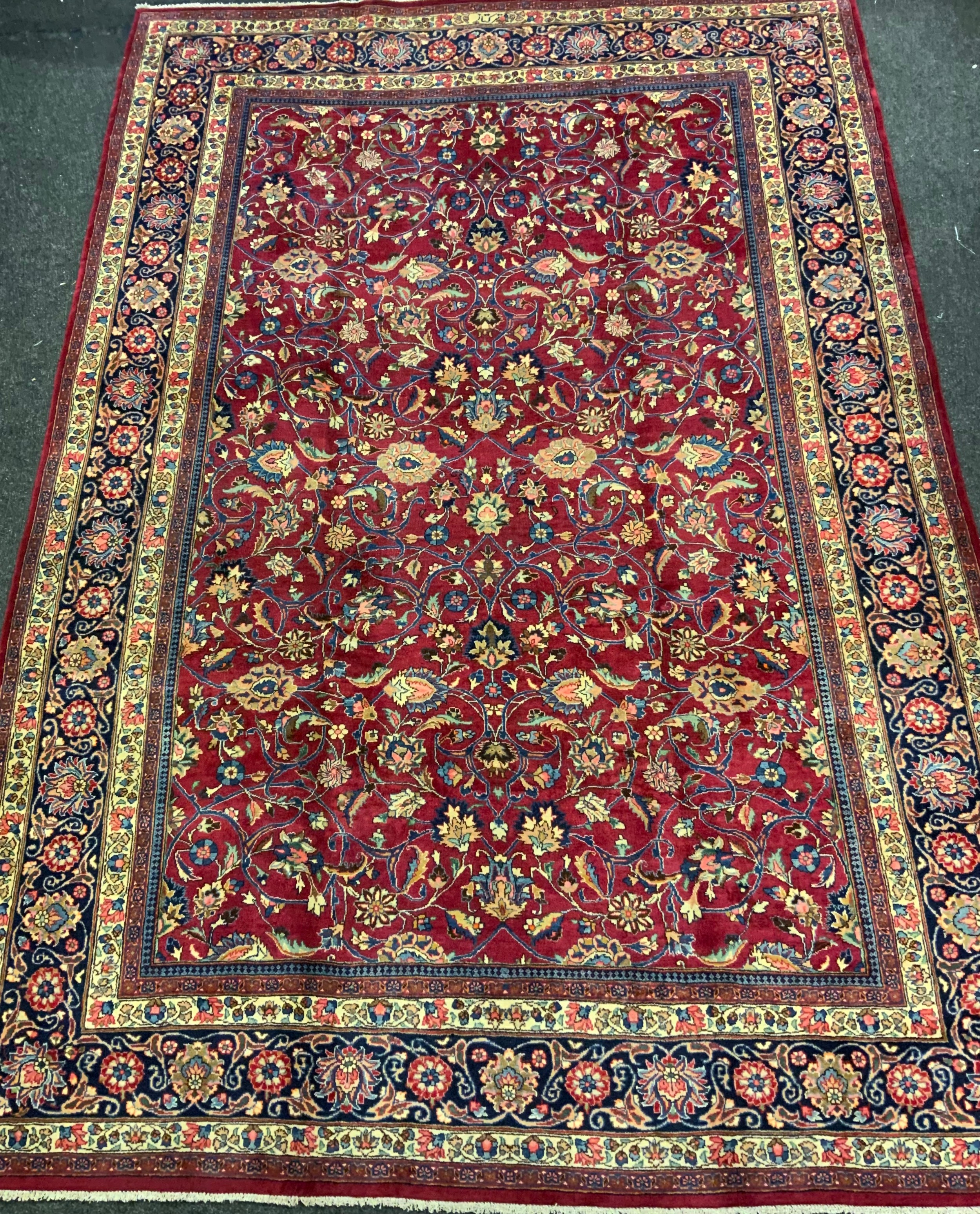 A Persian Tabriz hand-knotted rug / carpet, the field in rich red with scrolling tendrils of