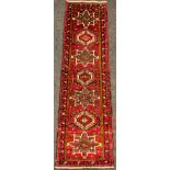 A North West Persian Heriz runner, hand-knotted in tones of red, black, blue, and cream, 275cm x