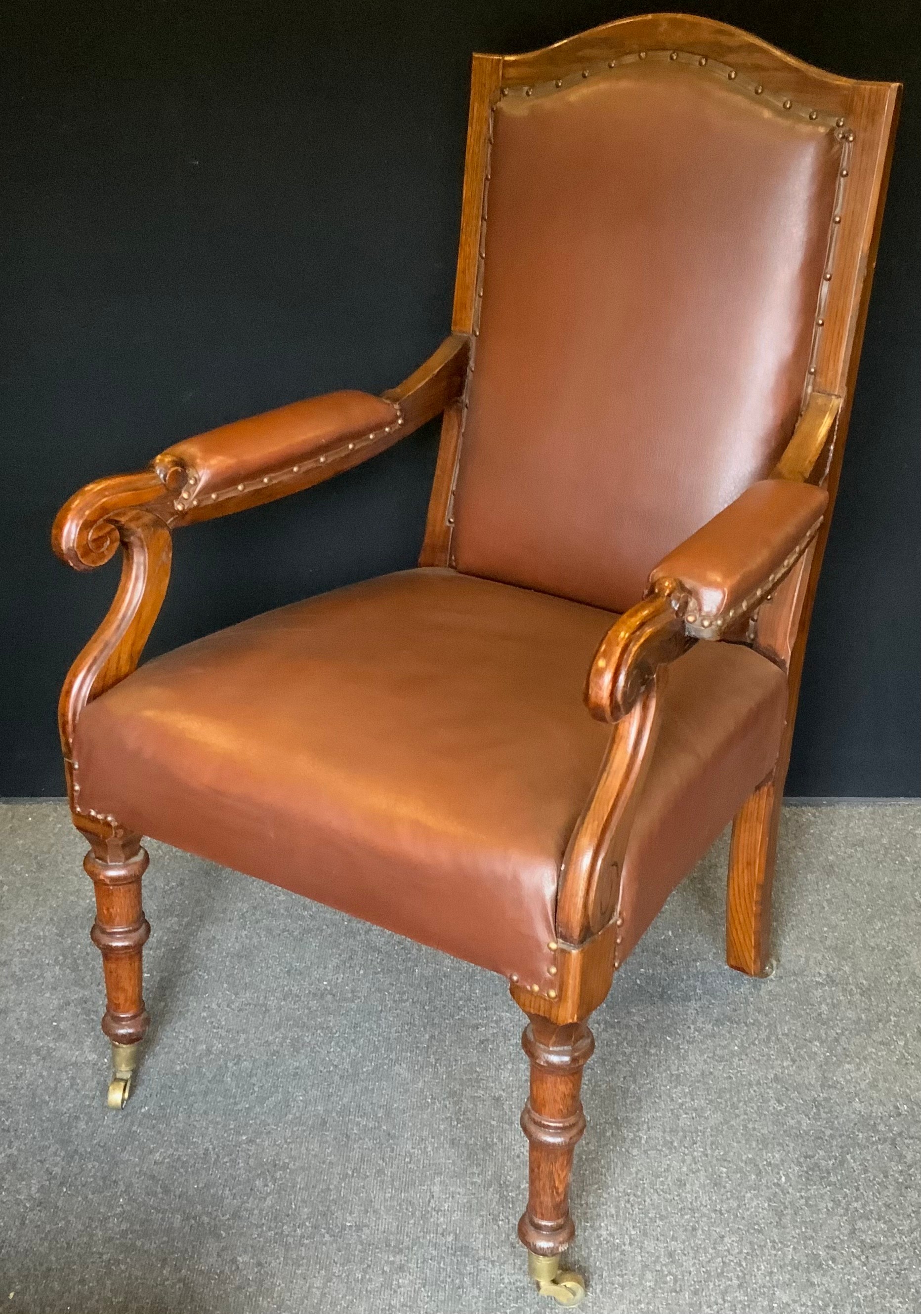 A Victorian oak Library arm chair, tan leather upholstered back, arms and seat, scroll arms,