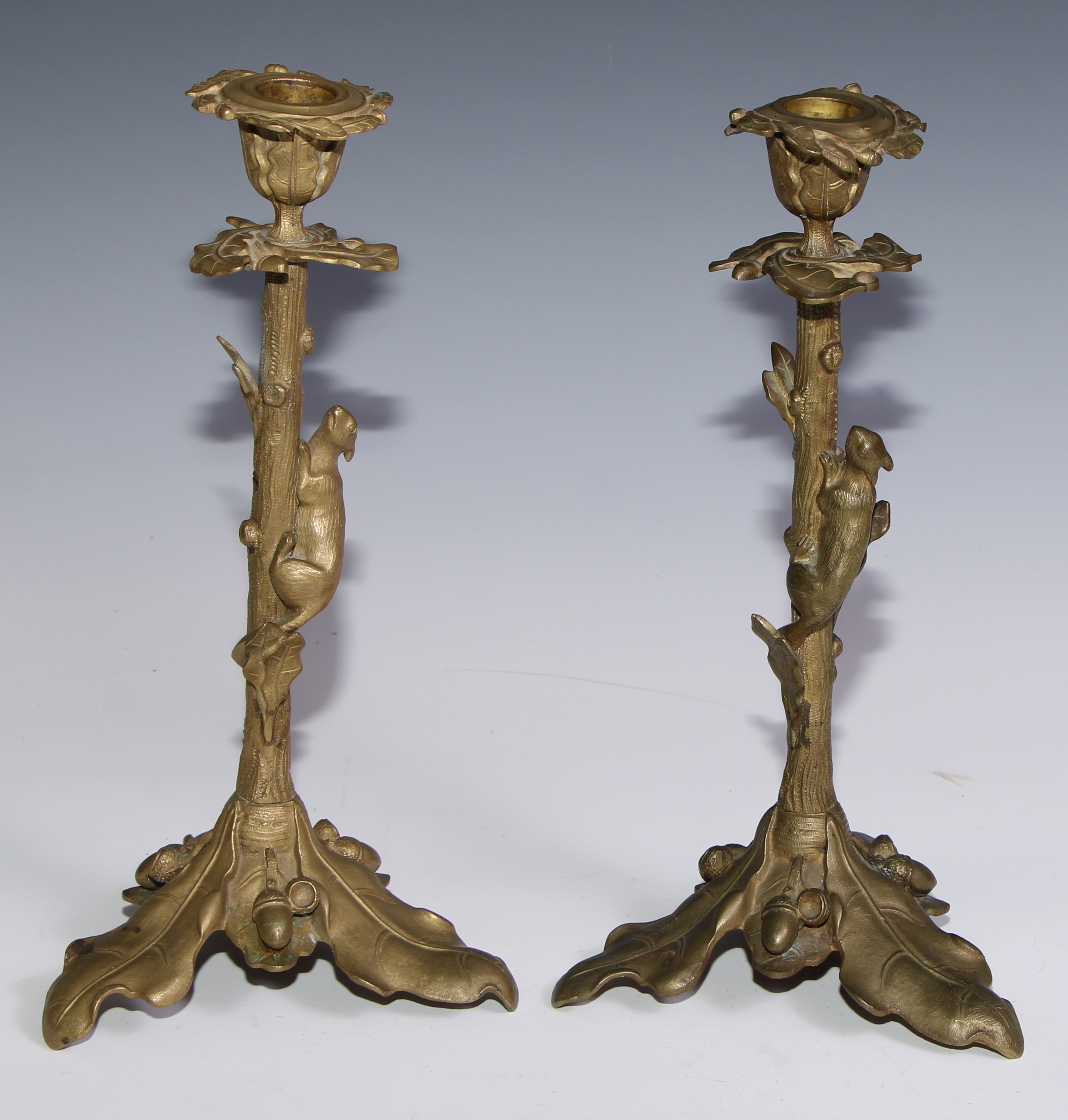 A pair of French gilt bronze candlesticks, cast with fruiting oak, each with a squirrel scaling