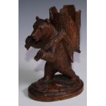 A Black Forest novelty spill holder, carved as a bear carrying a hollowed section of tree trunk,