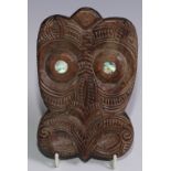 A Maori carving, after a koruru gable mask, carved with stylized features in reference to an