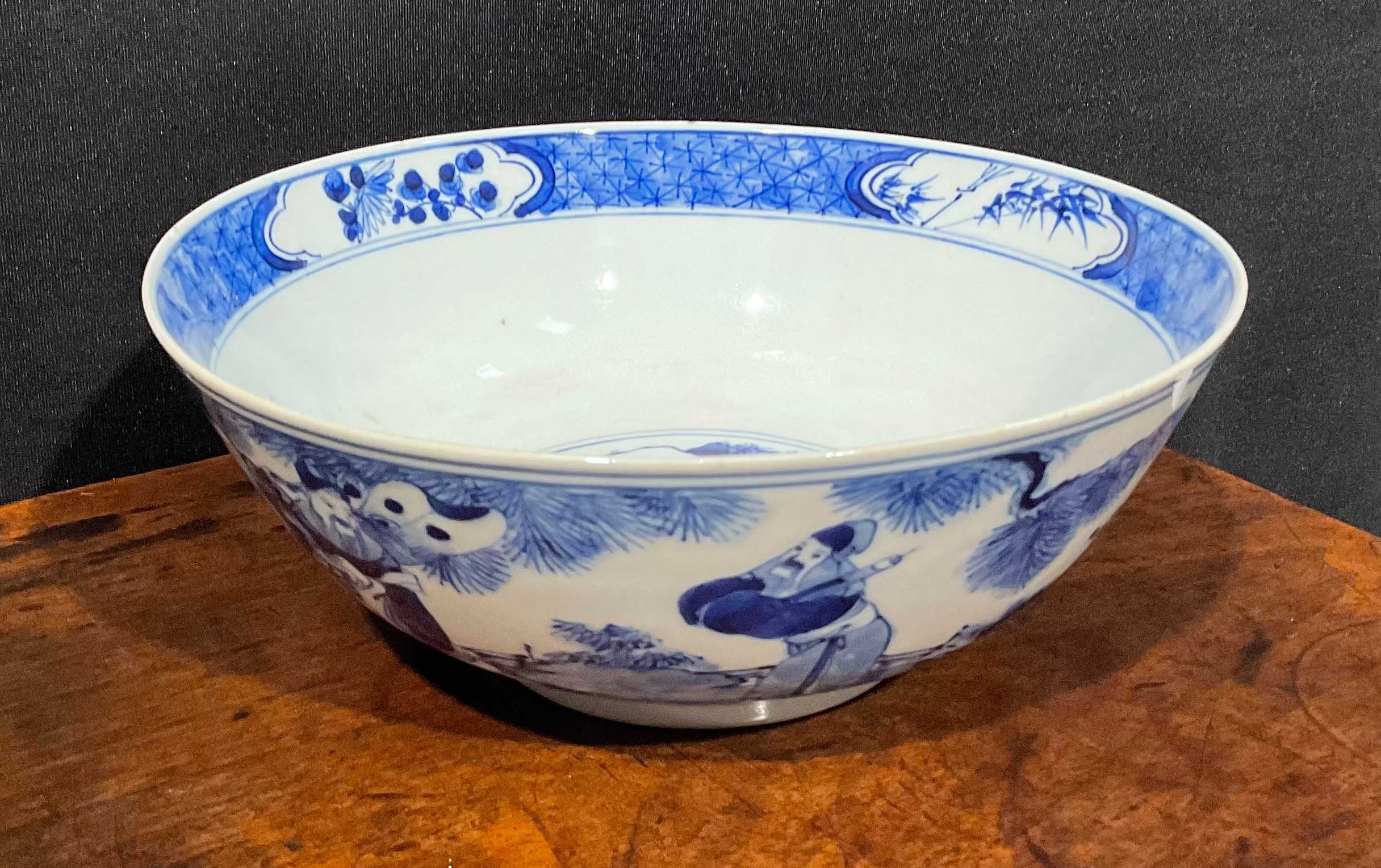 A Chinese circular bowl, playing in tones of underglaze blue with figures in a monumental landscape,