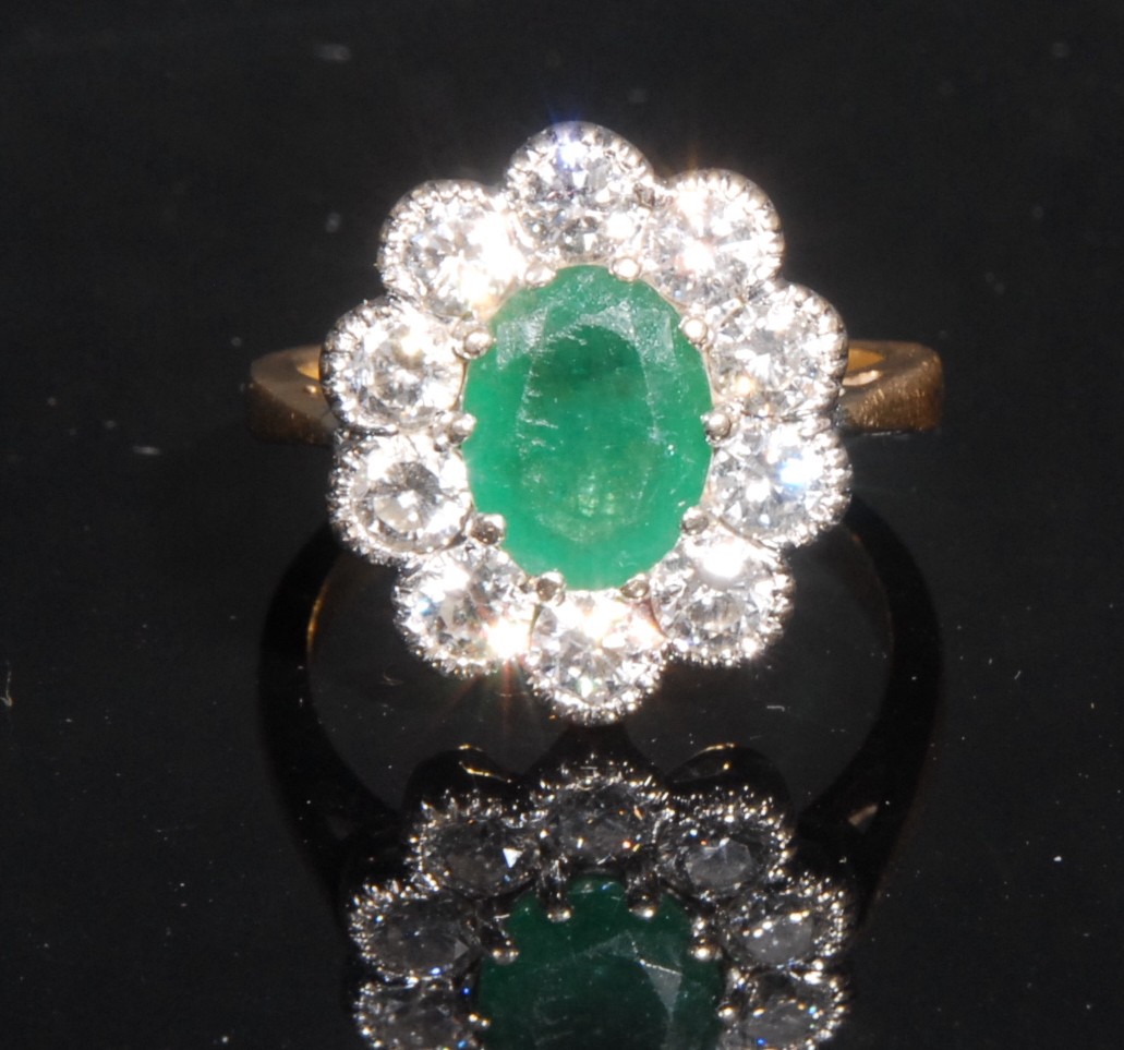 A diamond and emerald cluster ring, the central oval facet cut raised claw set emerald within 10