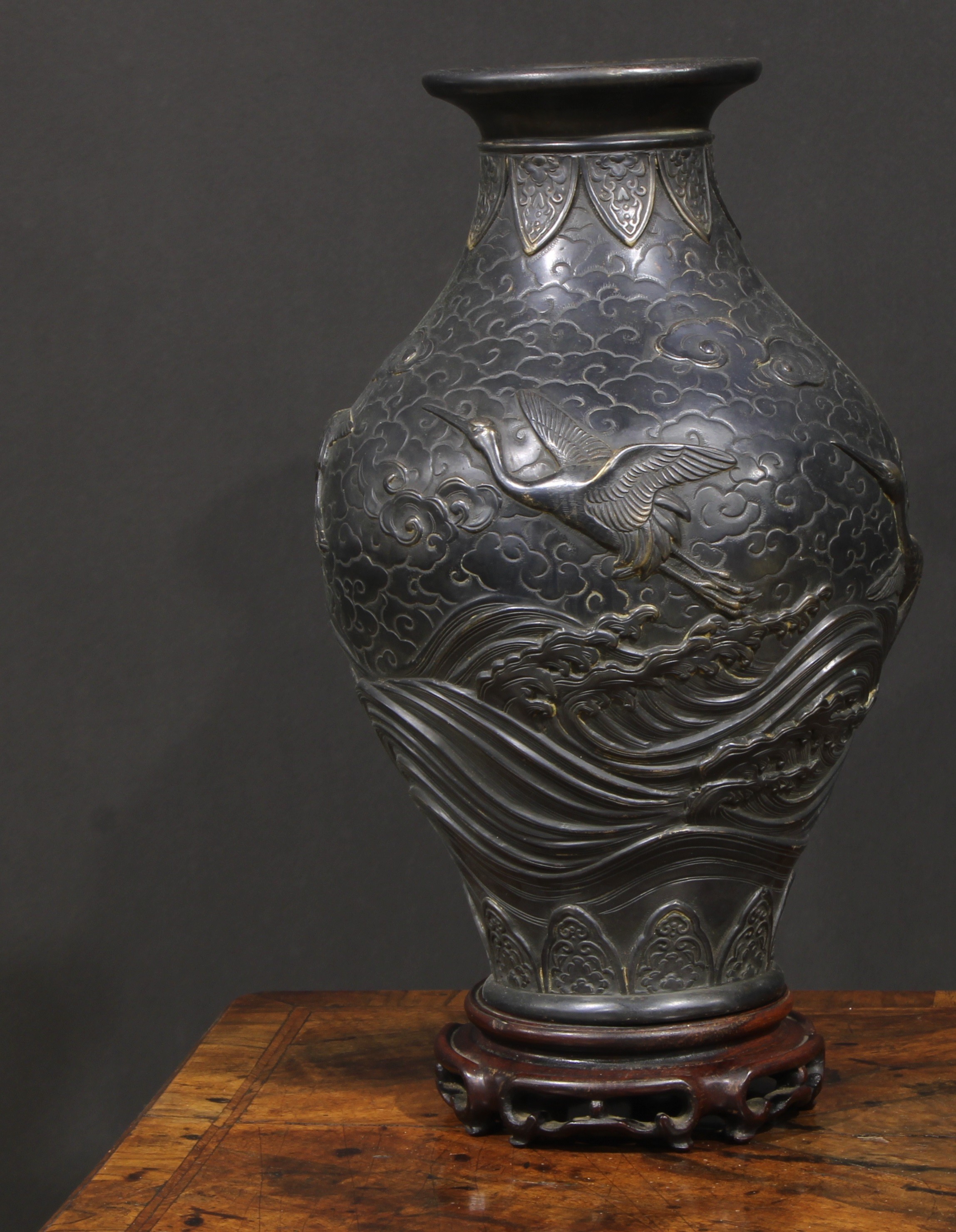 A Japanese dark patinated bronze ovoid vase, cast in relief with cranes taking flight amongst