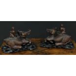 A pair of Chinese hardwood carvings, of boys riding buffalo, glass eyes, bone teeth, carved bases,