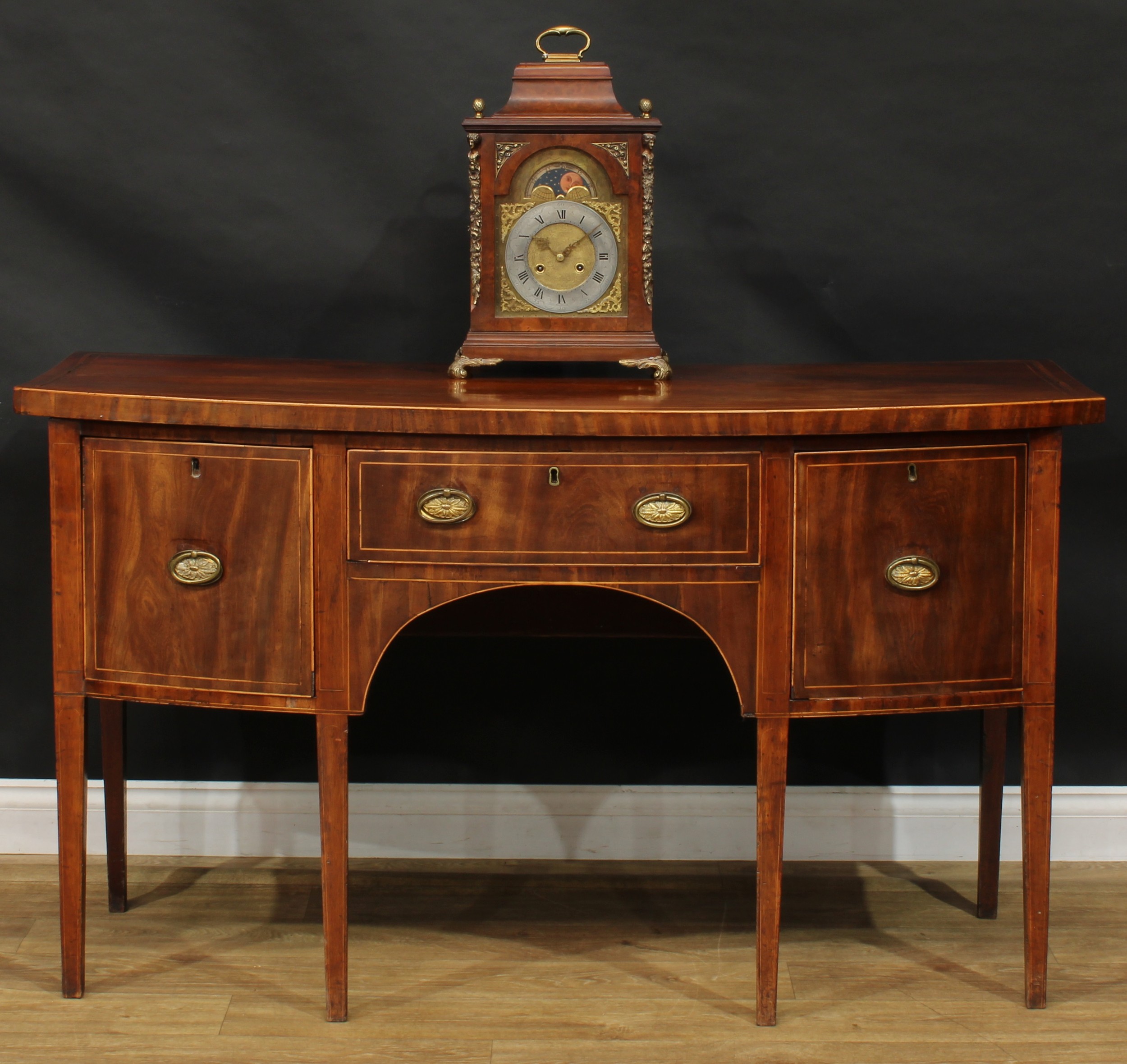 A George III mahogany bowfront sideboard or serving table, oversailing satinwood banded top above