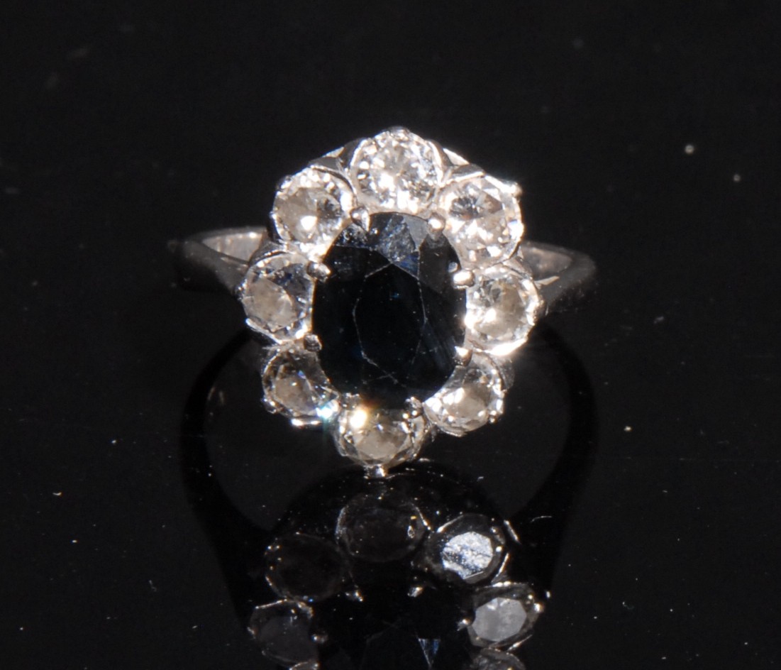 An 18ct white gold sapphire and diamond flowerhead cluster ring, the central oval cut sapphire 8mm x