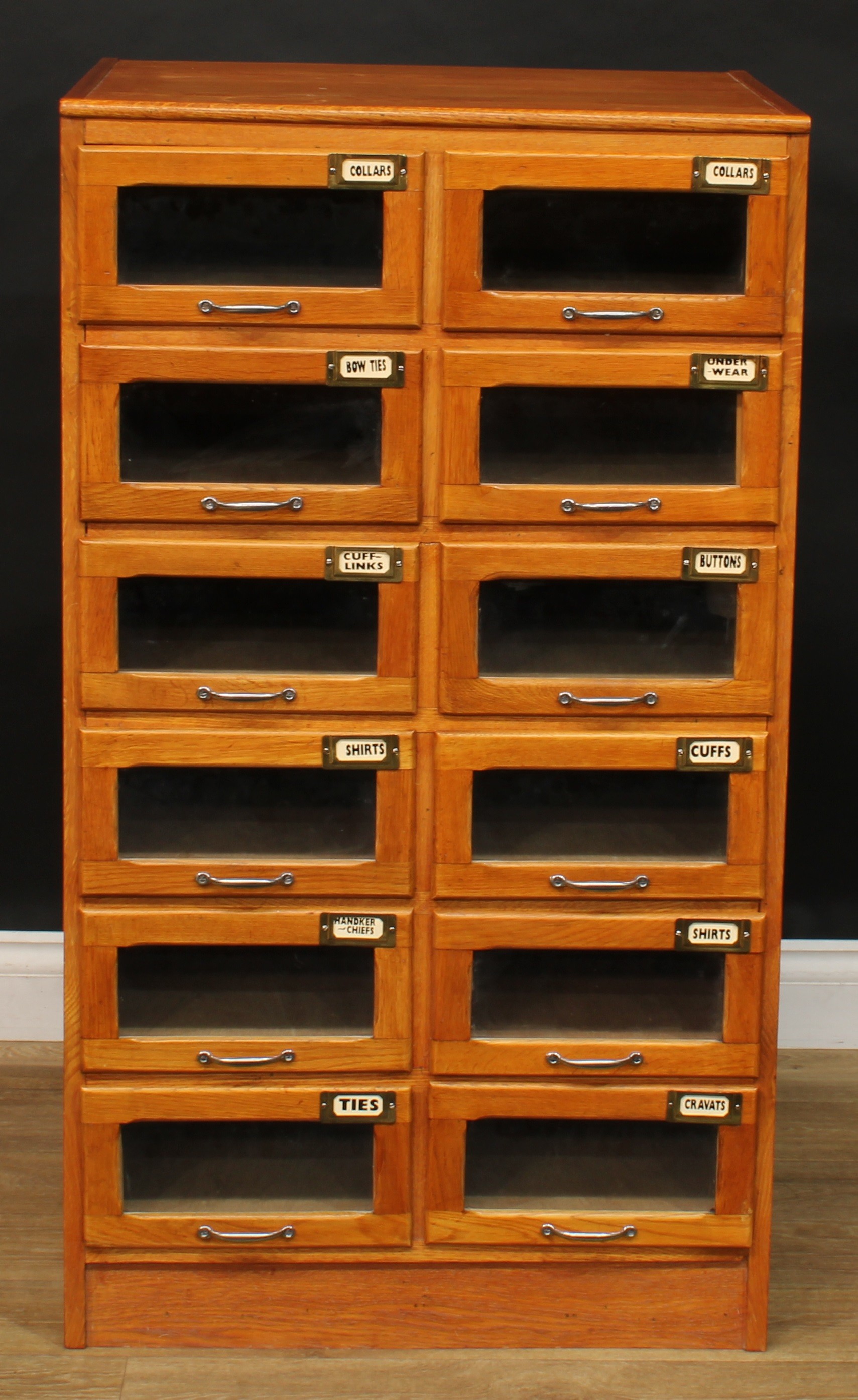 An early to mid 20th century oak haberdashery shop display chest, rectangular top above twelve