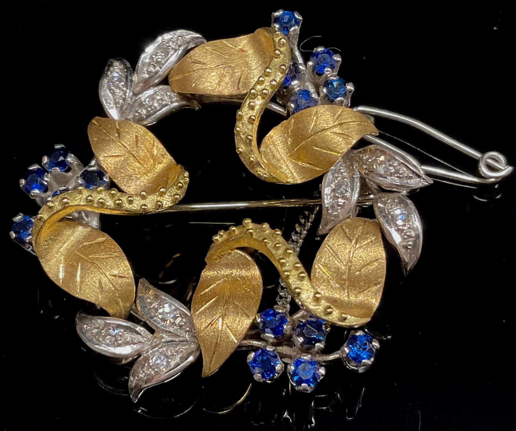 An 18ct white and yellow gold wreath brooch, formed from intertwined flowering stems and leaves, the