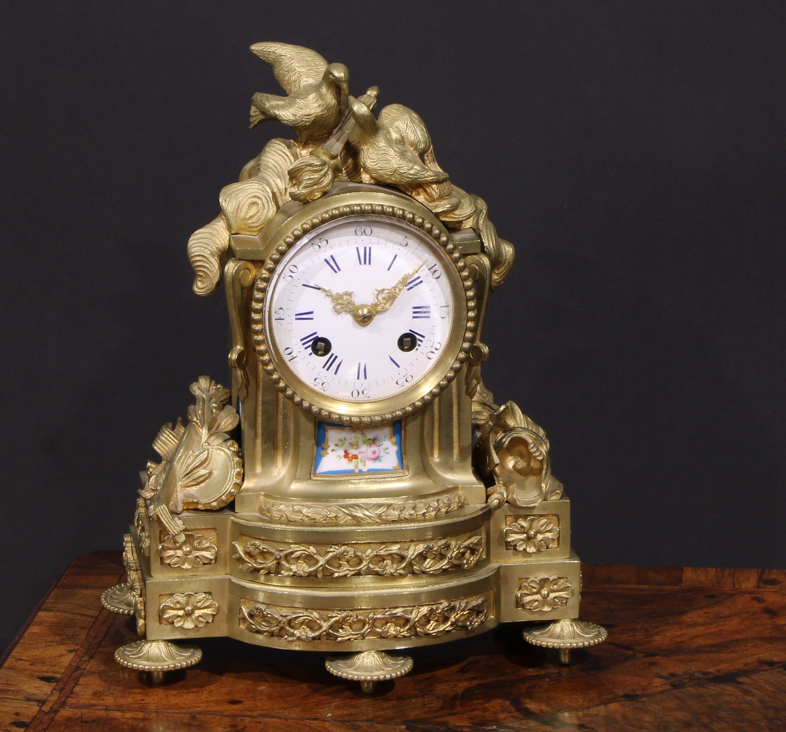 A French gilt brass mantel clock, crested with a pair of lovebirds and flaming torch, the white