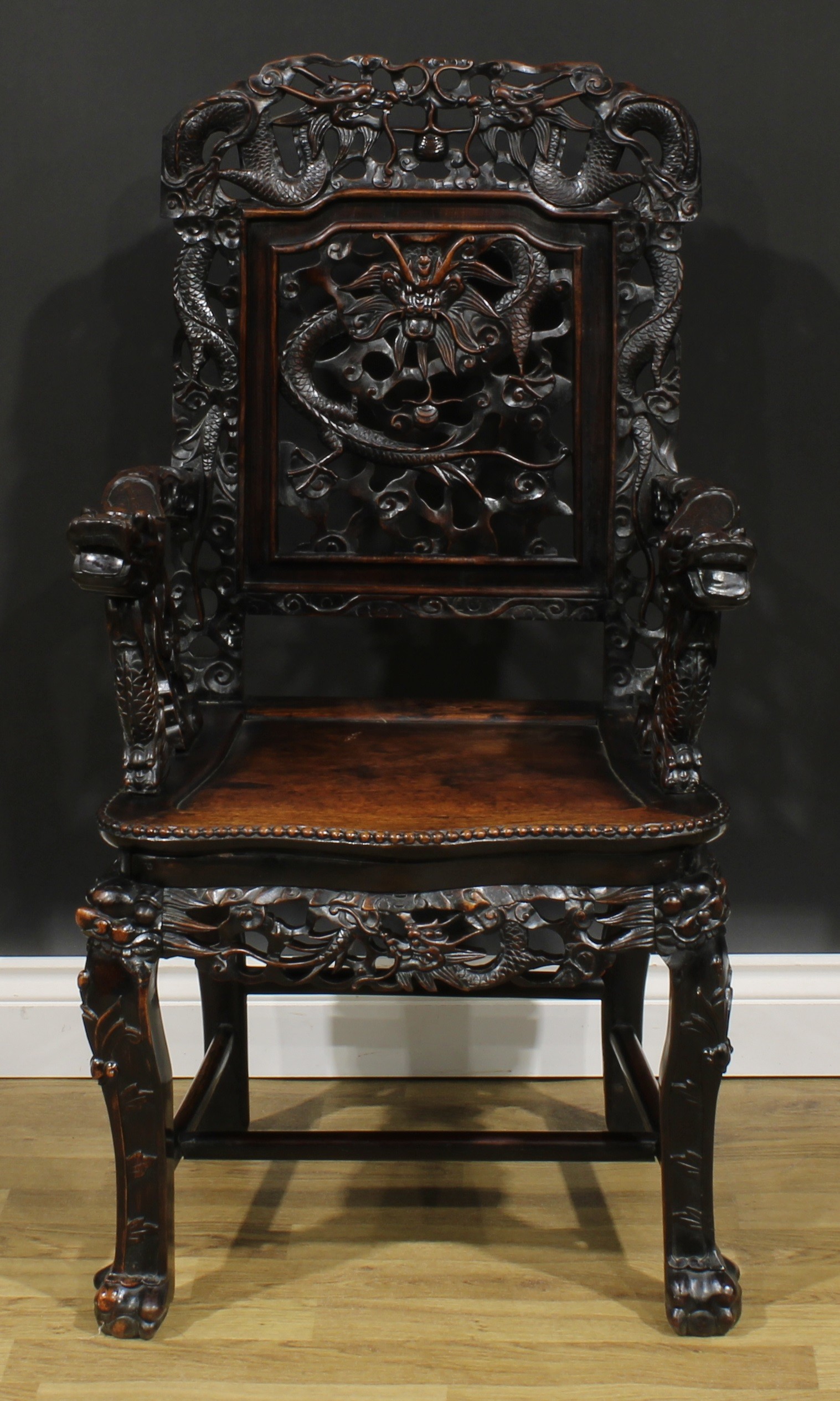 A Chinese hardwood armchair, carved throughout with dragons, serpentine seat with beaded border,