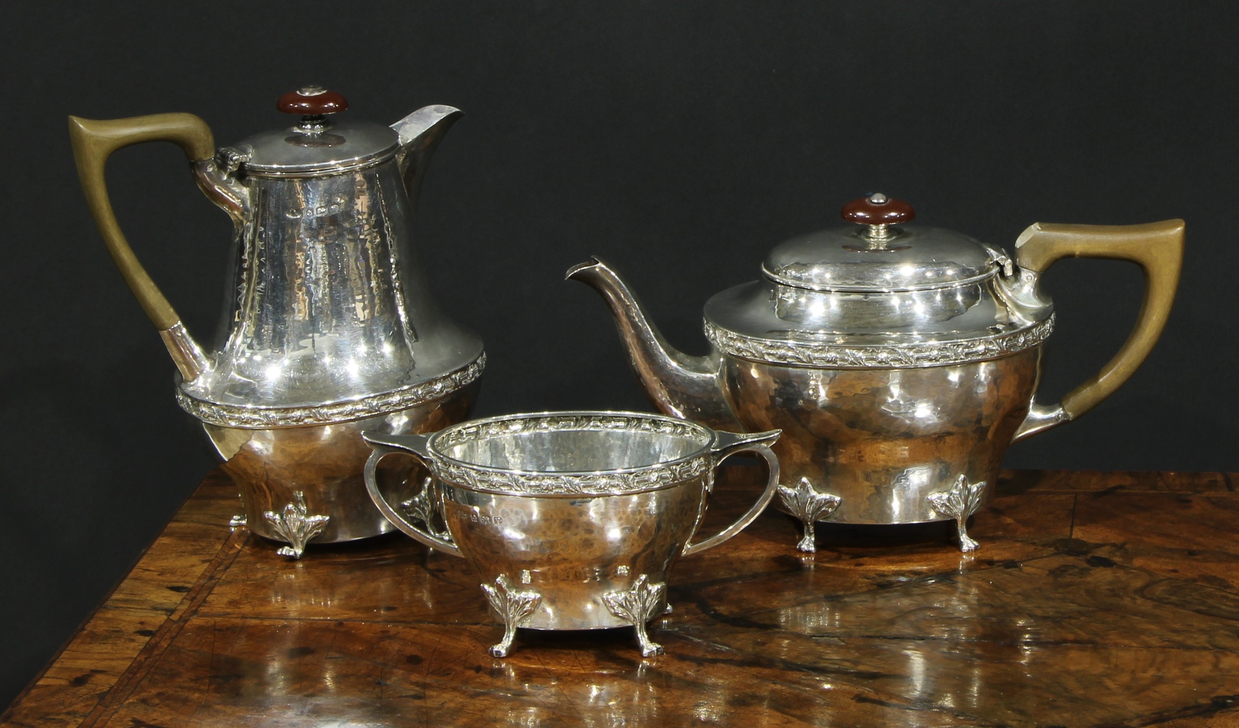 An Arts and Crafts silver three piece tea service, comprising teapot, hot water pot and sugar basin,