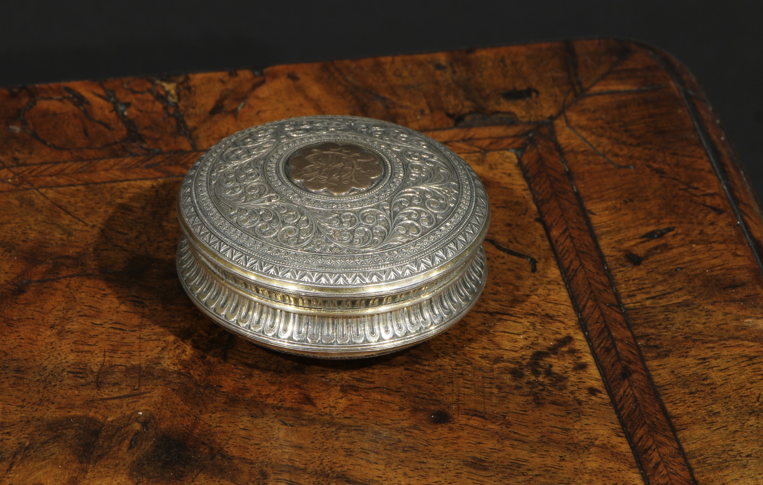 A 19th century silver and gold coloured metal circular snuff box, chased overall in the Indian