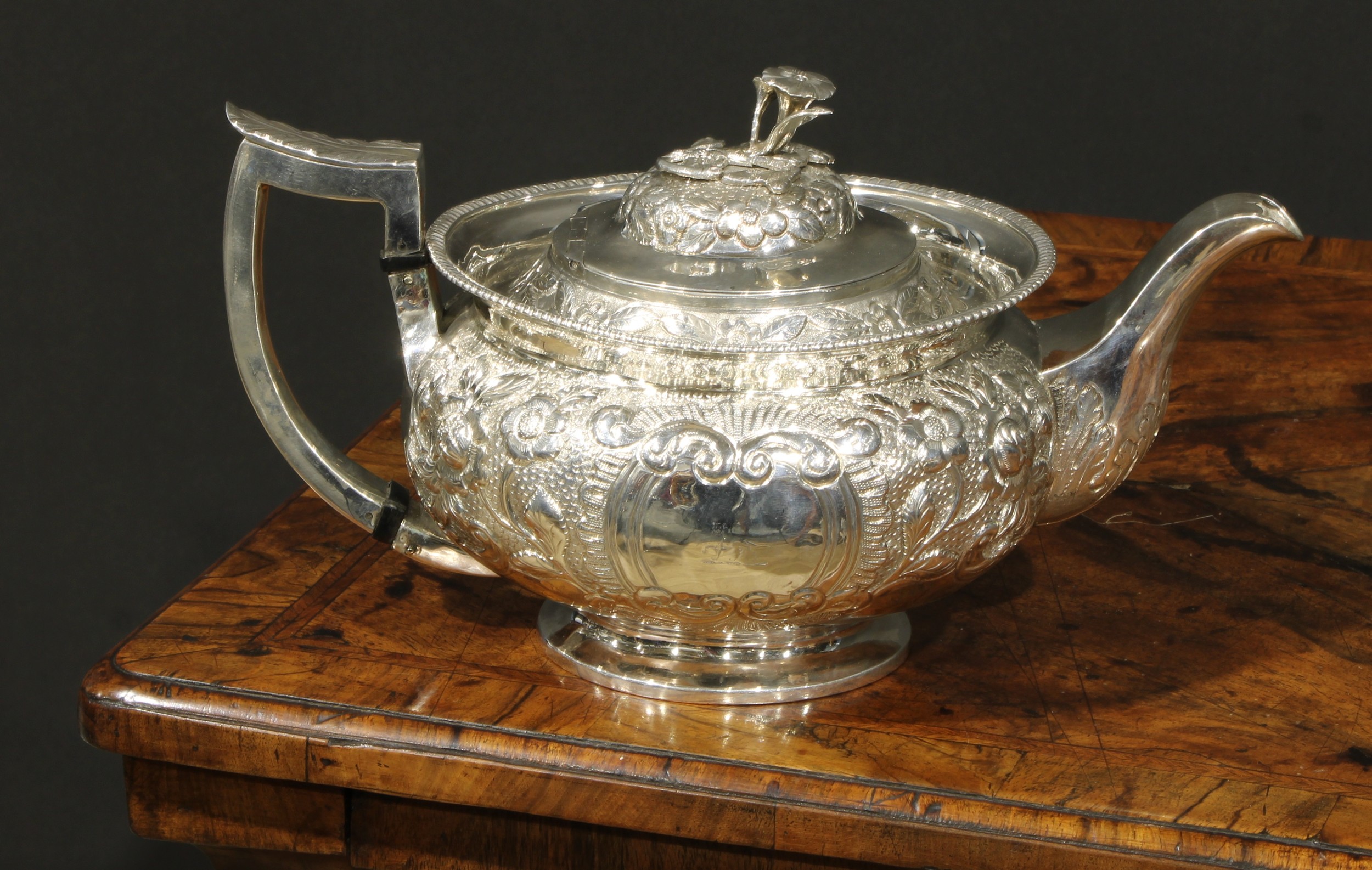 A George III Irish silver teapot, chased with chased with flowers and stiff leaves on a scale