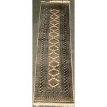 A Middle Eastern Bokhara type rug / carpet, knotted in muted tones, with a central row of diamond-