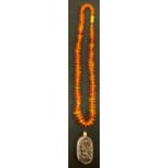 An oriental copal amber and silver coloured metal table let pendant necklace, carved and moulded
