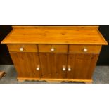 A pine sideboard, three short drawers to frieze, above three cupboard doors, white ceramic knobs,