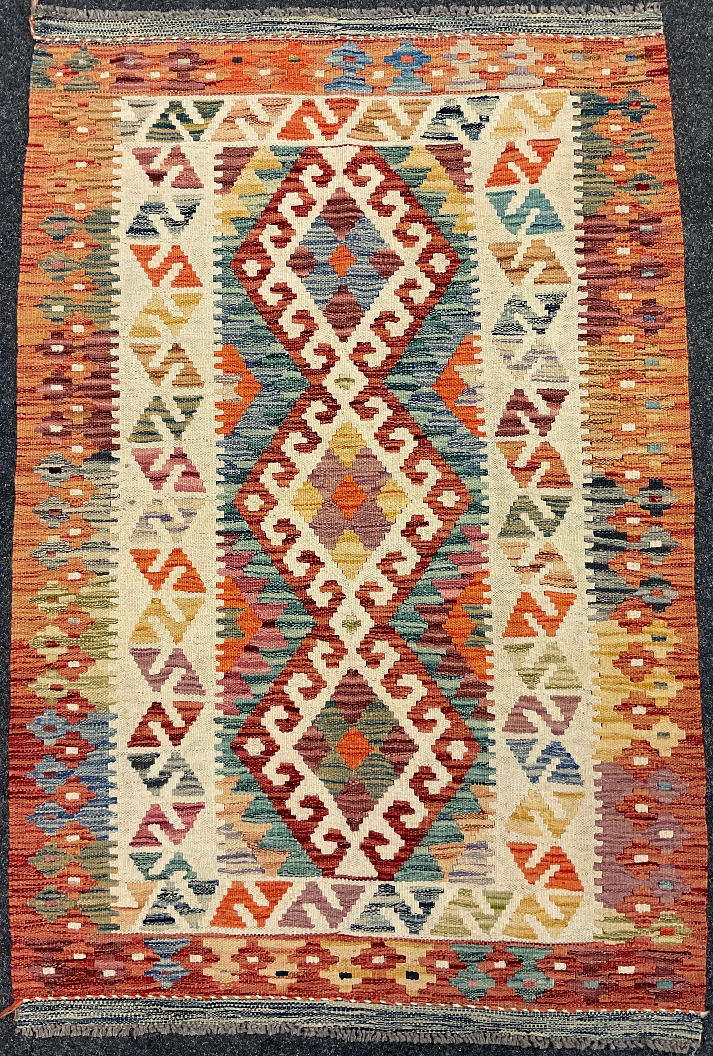 A Turkish Anatolian Kilim rug / carpet, knotted in bright tones of red, orange, green, and cream,