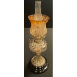 An early 20th century oil lamp, clear glass font, spreading brass column on black glazed pedestal