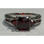 A 10kt white gold ring, set with a princess cut garnet, the shoulders with channel set garnets, ring