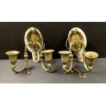 A pair of gilt brass two branch wall sconces, the oval back plates surmounted with ram masks and