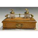 A blonde oak desk standish, brass gallery, pair of clear glass inkwells, mounted with brass eagle