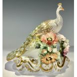A Royal Crown Derby Peacock, perched upon a bough encrusted with flowers, scroll base, printed