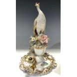 A Royal Crown Derby Peacock, neck extended, seated upon a floral encrusted urn quatrefoil base,