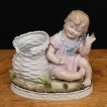 A late 19th century German bisque piano baby spill vase, modelled as a seated young girl alongside a